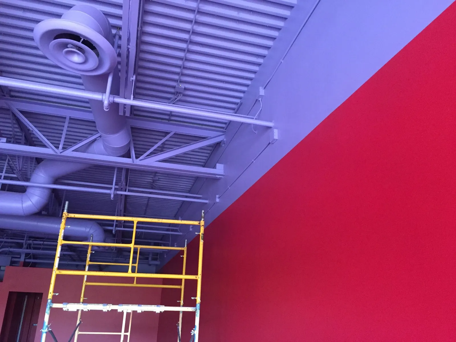 Commercial interior with an exposed ceiling painted out and a red accent wall, scaffolding in place